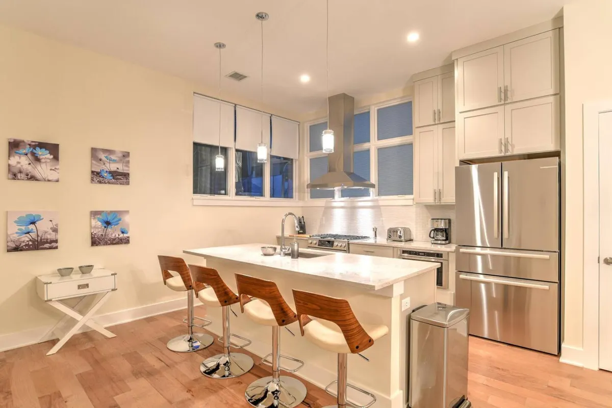 A contemporary kitchen with an inviting island countertop surrounded by bar stools, sleek appliances, and vibrant wall art. The space is bright and social, hinting at opportunities for entertaining and casual dining before a night out.