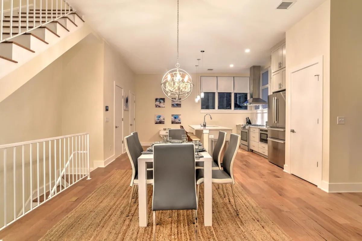 A stylish and comfortable dining area with a large table, elegant chandelier, and open kitchen space in the background. The design balances sophistication with a family-friendly touch, making it ideal for shared meals or casual gatherings.