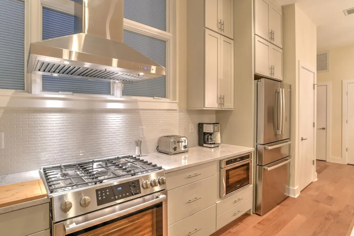 A sleek, fully equipped kitchen with stainless steel appliances, a gas stove, white cabinetry, and a marble countertop. The space exudes both modern functionality and warmth, ideal for preparing meals after exploring the city or for extended stays.