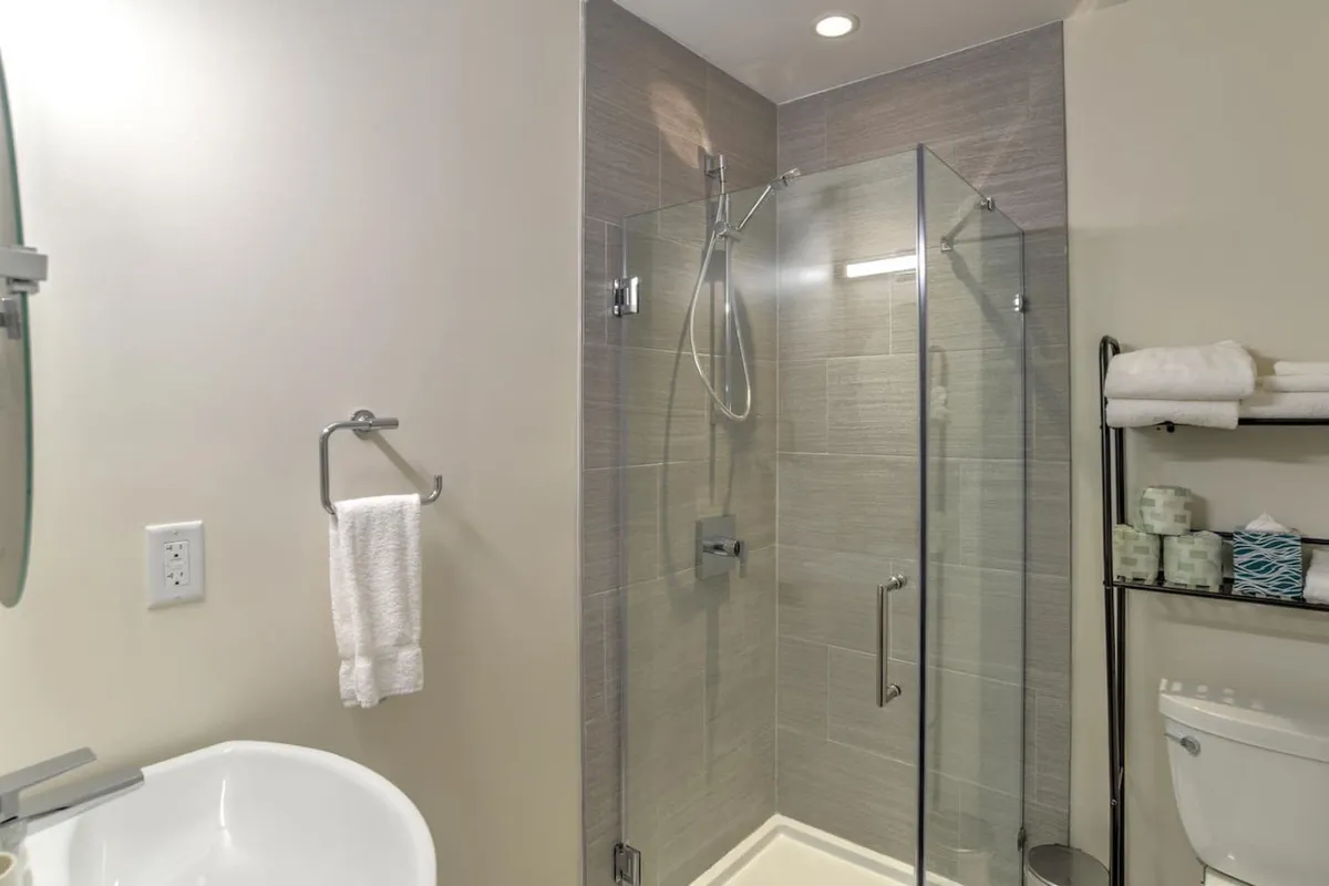 A modern bathroom featuring a glass shower enclosure, a sleek sink with contemporary fixtures, and fresh towels arranged neatly. The space is bathed in soft light, highlighting high-end finishes and a serene, spa-like atmosphere.