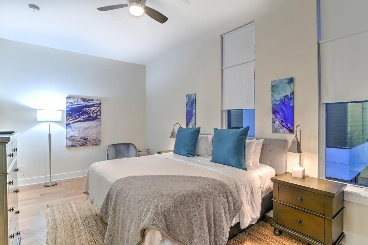 A cozy bedroom with a plush bed, soft lighting from a bedside lamp, and artistic accents on the walls. The space feels intimate and inviting, perfect for unwinding after a busy day.