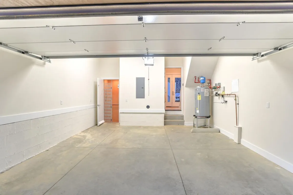 A view into a clean, organized garage featuring a closed garage door, a water heater mounted on the wall, and stairs leading directly into the home. The space is tidy and practical, with ample room for parking and storage.