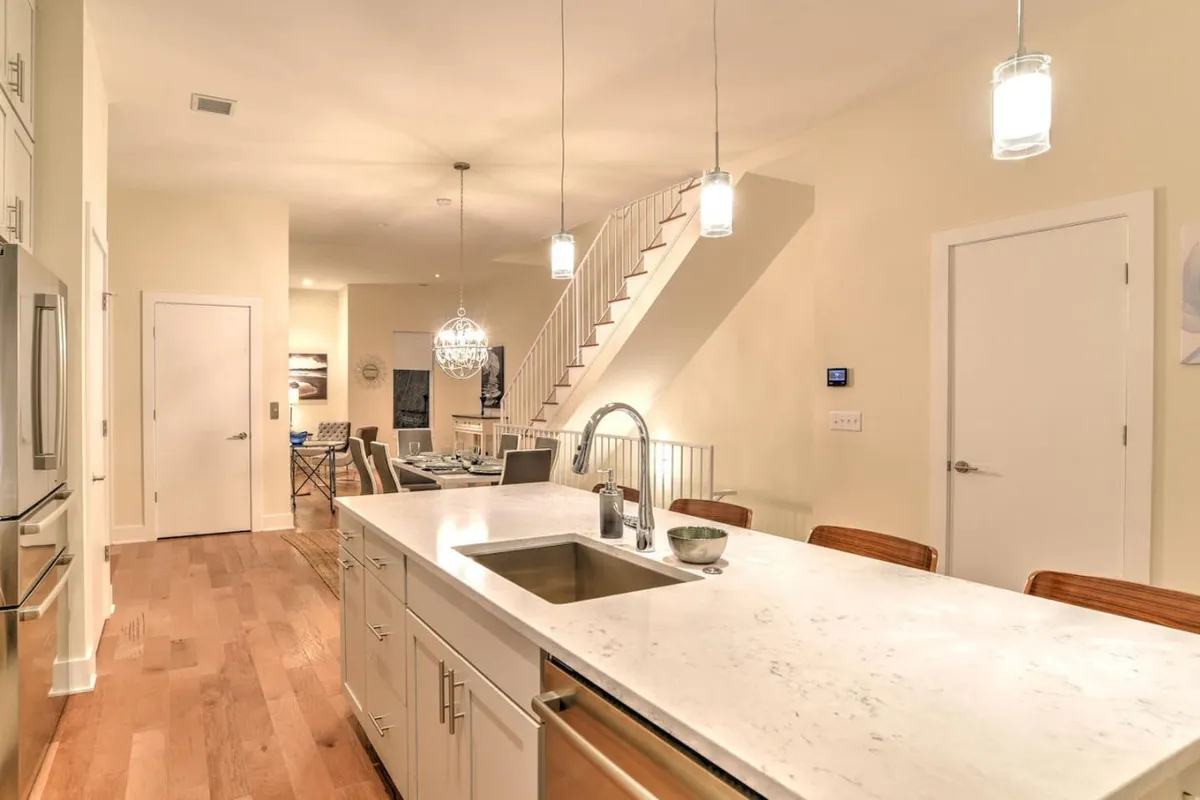 A welcoming and functional kitchen space featuring a large island, a modern chandelier, and a staircase leading to other levels of the home. The layout invites gatherings and casual conversation, highlighting an open and airy atmosphere.