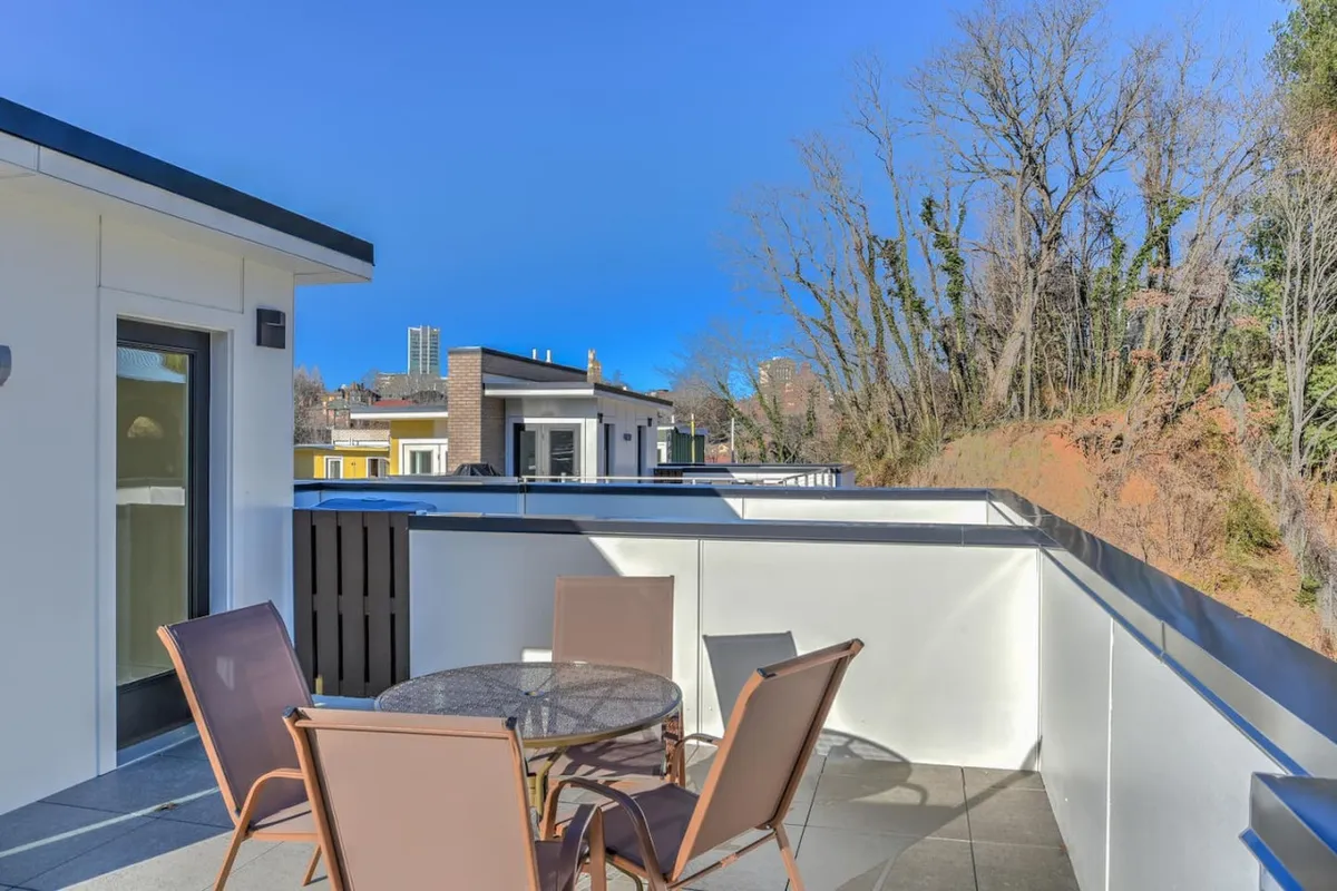 This exterior image features another outdoor seating area with a round table surrounded by greenery, ideal for socializing, morning coffee, or evening relaxation. The greenery and open-air design create a versatile space for both quiet moments and gatherings.